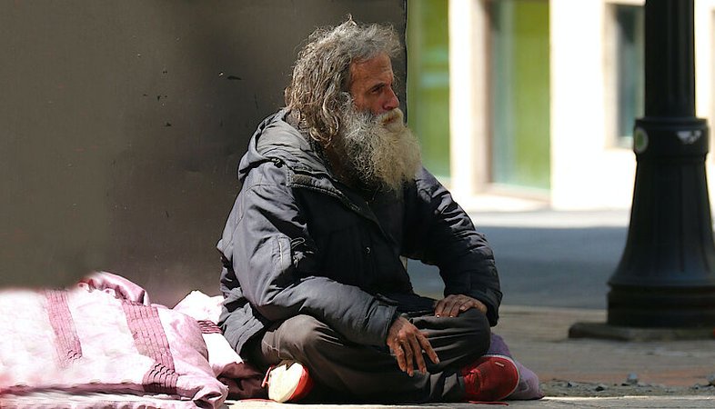Ein Obdachloser im Schneidersitz auf der Straße